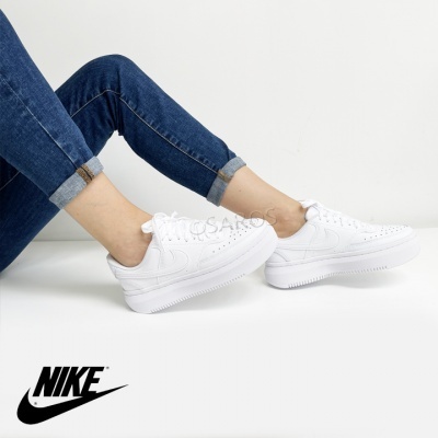 Ténis Nike brancos usados por pessoa com calças de ganga azul escuro