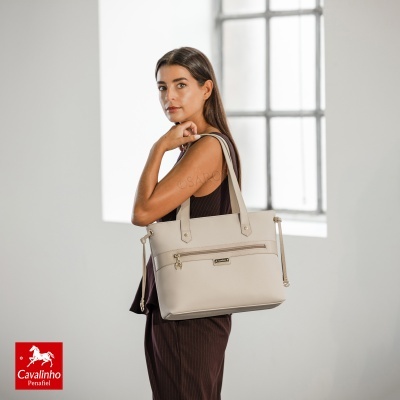 Mala de senhora bege com alças longas e bolso frontal, transportada por mulher com vestido castanho.