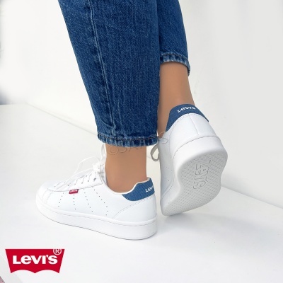 Ténis brancos Levi's com detalhes azuis no calcanhar e etiqueta vermelha, usados com calças de ganga azuis
