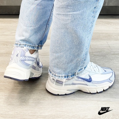 Ténis Nike brancos com detalhes lilás e azul, usados com calças de ganga azul.