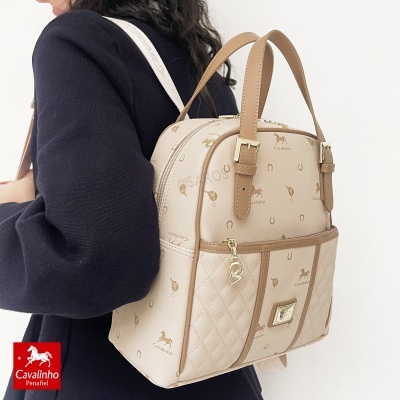 Mochila Cavalinho bege com padrão castanho e detalhes dourados usada por pessoa com casaco preto