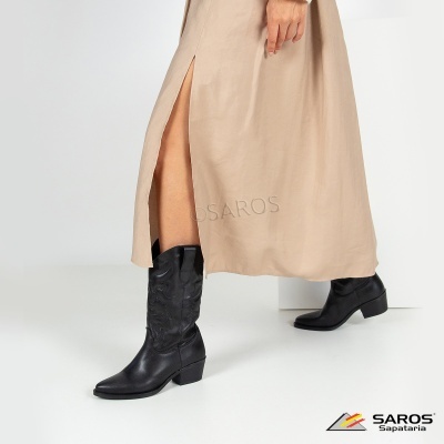 Botas pretas em pele com vestido bege e fenda, fundo branco, logótipo SAROS Sapataria