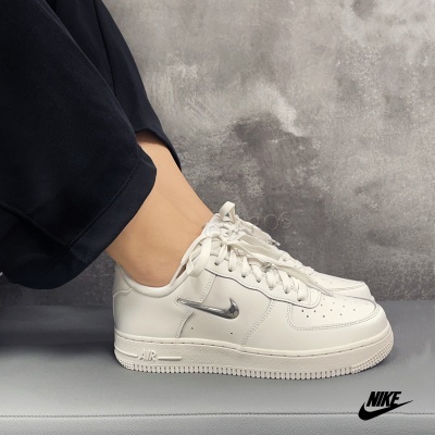 Tênis Nike Air Force 1 brancos com logo prateado e sola branca em fundo cinzento