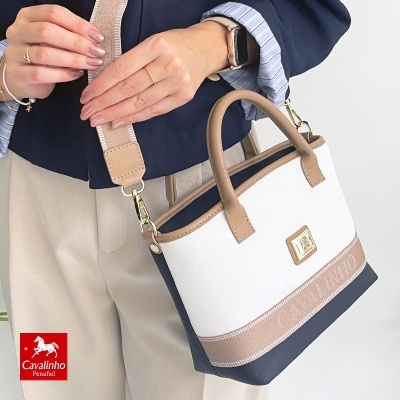 Mala de mão feminina em tecido branco com detalhes bege e azul escuro, alça ajustável e placa metálica CAVALINHO.