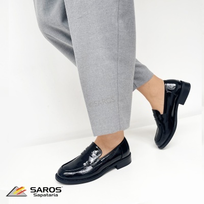 Sapatos mocassim pretos brilhantes em pele com calças cinzentas.