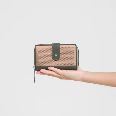 Carteira de pele rosa e verde-escura com padrão perfurado e fecho, segura por mão feminina