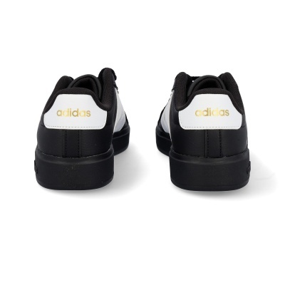 Ténis Adidas pretos e brancos vistos de trás com logo dourado na parte de trás.