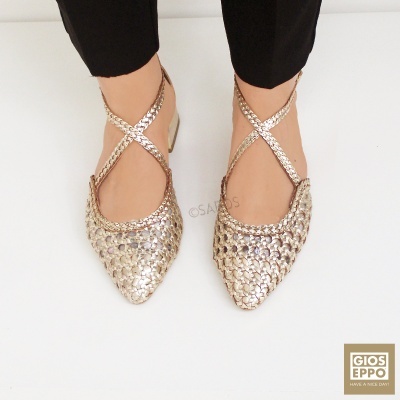 Sapatos rasos dourados com tiras cruzadas em fundo branco