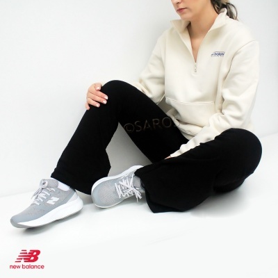 Pessoa com casaco branco NEW BALANCE, calças pretas e sapatilhas cinza e brancas.