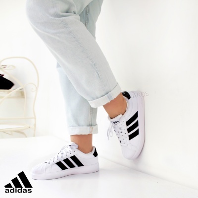 Ténis Adidas branco com riscas pretas usados com calças de ganga claras.