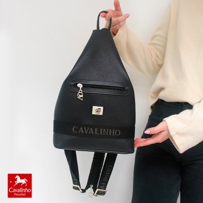 Mochila preta com logótipo Cavalinho e faixa bordada a ser segurada por pessoa com camisola creme.
