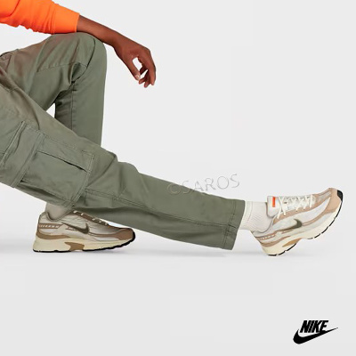 Pessoa com calças cargo verdes e ténis Nike bege e branco sentada num fundo cinzento.