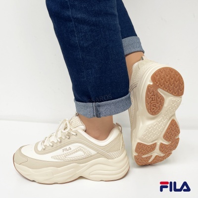 Ténis Fila bege e branco com sola castanha usados com calças de ganga azul