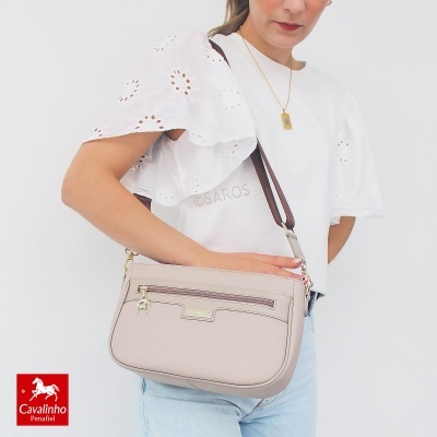 Mala de ombro bege claro com fecho de correr e alça castanha, usada por modelo com blusa branca e calças azuis claras