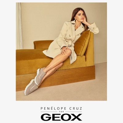 Mulher com trench coat bege e sapatos cinza sentada em sofá amarelo.