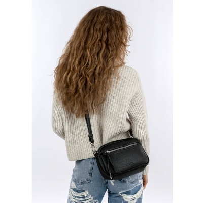 Pessoa com camisola bege, jeans rasgados e mala preta de pele ao ombro
