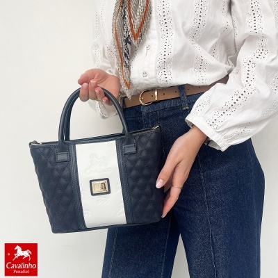 Mala de mão preta e branca com logotipo Cavalinho segurada por pessoa com camisa branca e jeans