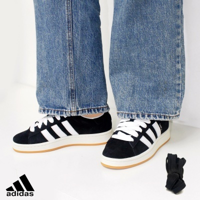 Ténis Adidas pretos com riscas brancas e sola clara usados com calças de ganga azuis