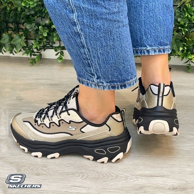 Ténis Skechers bege, branco e preto usados com calças de ganga azul.