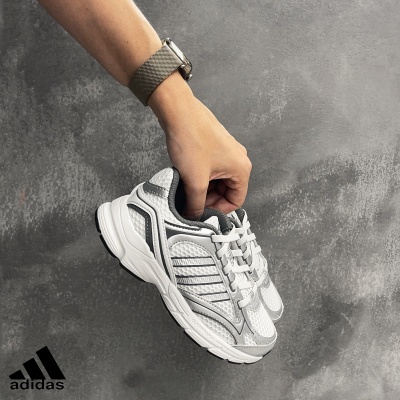 Ténis desportivos Adidas brancos e cinza segurados por mão com relógio