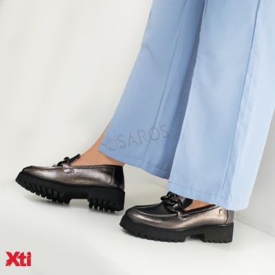 Sapatos femininos pretos metálicos com sola grossa e laços, calças azuis claras, fundo branco