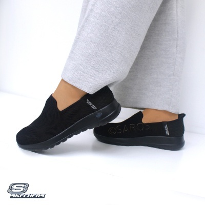 Sapatos desportivos Skechers pretos usados com calças cinzentas.