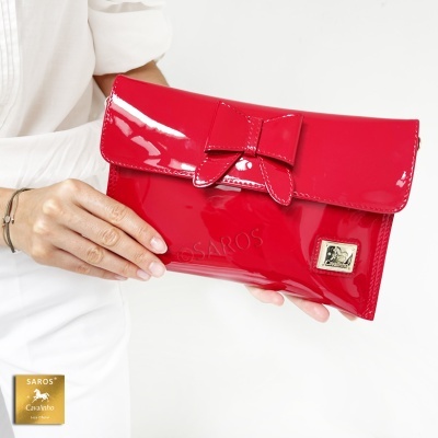 Carteira vermelha em verniz com laço e placa metálica, segurada por pessoa de roupa branca