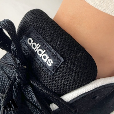Ténis Adidas preto com etiqueta visível e atacadores pretos próximo ao tornozelo