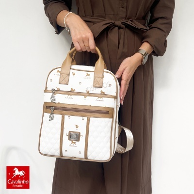 Mala mochila branca com padrão Cavalinho, detalhes castanhos, em mãos de pessoa com vestido castanho