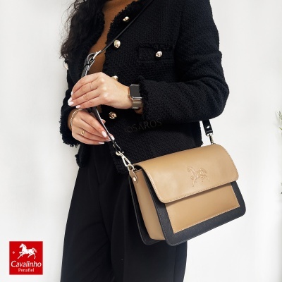 Mala de ombro Cavalinho camel e preta com gravura de cavalo, mulher com casaco preto e relógio smart