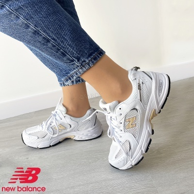 Tênis New Balance branco com detalhes bege e cinza usados com calças de ganga azul