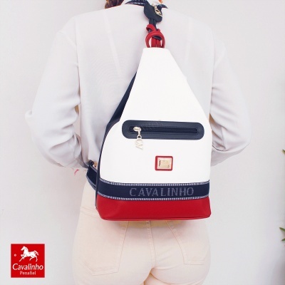 Mochila branca, azul escuro e vermelha com detalhes em metal, usada nas costas por pessoa de branco.