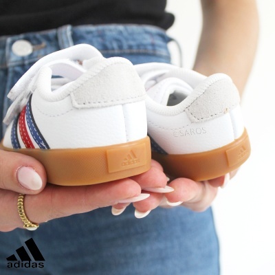 Ténis Adidas brancos com sola castanha e detalhes coloridos, segurados por mãos femininas