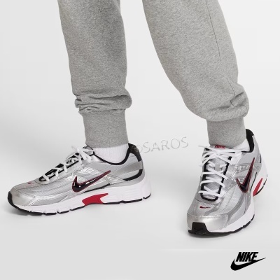 Ténis desportivos Nike prateados com detalhes vermelhos e pretos usados com calças cinza.