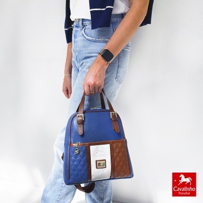 Mala azul, branca e castanha com padrão acolchoado, segurada por mulher com jeans e smartwatch