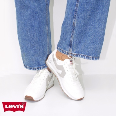 Sapatilhas brancas com detalhes cinza e sola castanha usadas com calças de ganga azuis, logótipo Levi's vermelho no canto inferior esquerdo.