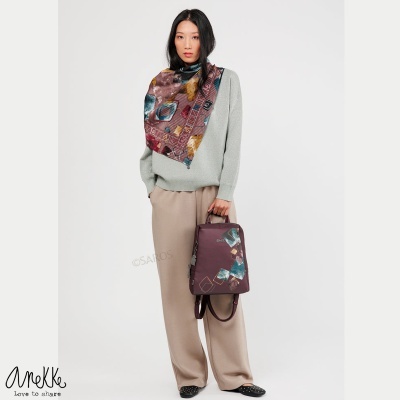 Mulher com lenço estampado e mochila castanha com padrão colorido, vestindo roupas casual cinzenta e bege