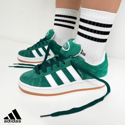 Ténis Adidas Campus verdes com riscas brancas e meias brancas às riscas pretas.
