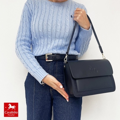 Mala preta de senhora em pele com relevo de cavalo e mulher com camisola azul, jeans e cinto preto