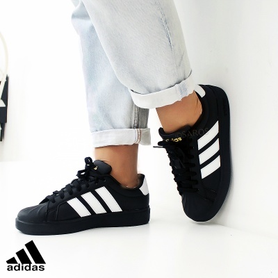 Sapatilhas Adidas pretas com riscas brancas e detalhes dourados, com calças de ganga claras