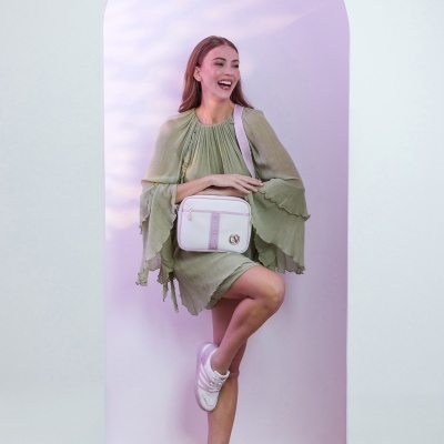 Mulher com vestido verde claro e mala branca com detalhes lilases