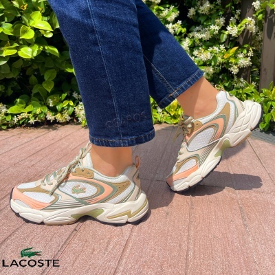 Ténis femininos Lacoste branco, bege, verde e salmão com sola espessa usados com calças de ganga azuis.