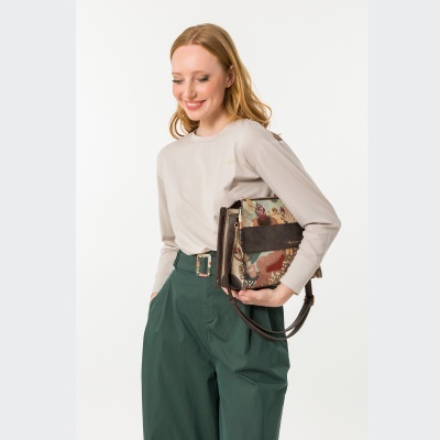 Mulher com blusa bege e calças verdes segurando mala floral castanha