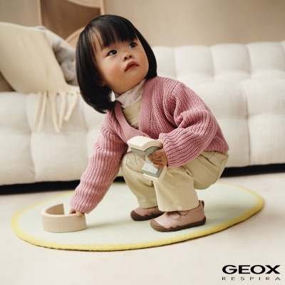 Criança com casaco rosa e sapatos cor de rosa a brincar num tapete amarelo claro