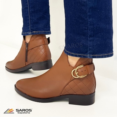 Botas ankle castanhas com fecho lateral e fivela dourada, usadas com calças de ganga azul