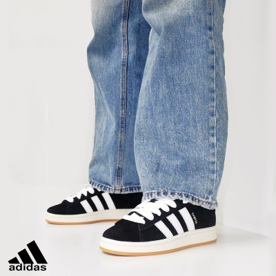 Ténis Adidas preto e branco com três riscas, solado castanho claro, usados com calças de ganga