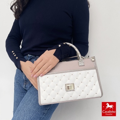 Mala de senhora branca acolchoada com rebites dourados e alças bege claro, com pessoa segurando e logo Cavalinho Penafiel