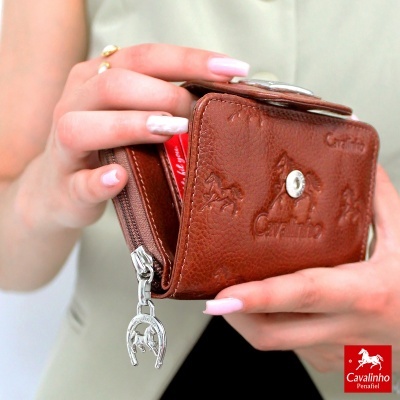 Carteira castanha de couro Cavalinho com relevos de cavalos e fecho de ferradura, segurada por mãos femininas