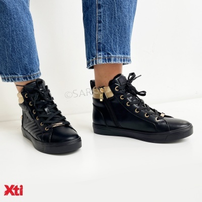 Ténis altos pretos com atacadores e detalhes dourados, visto com calças de ganga azuis.