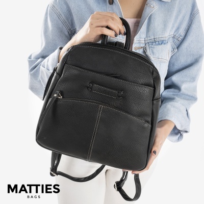 Mochila preta MATTIES em pele com costuras brancas segurada por pessoa com casaco de ganga.